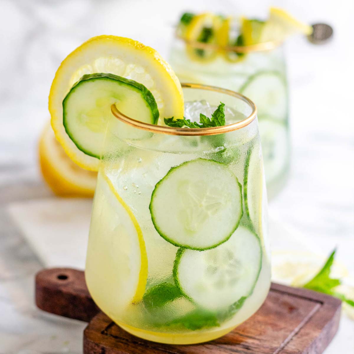 A cocktail garnished with lemon and cucumber slices and fresh mint.