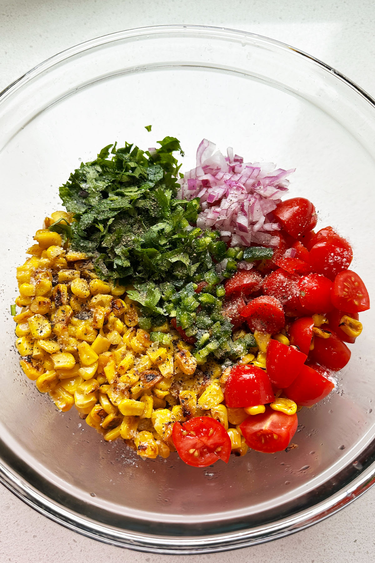 A bowl with charred corn, grape tomatoes, red onion, jalapeno, and cilantro.