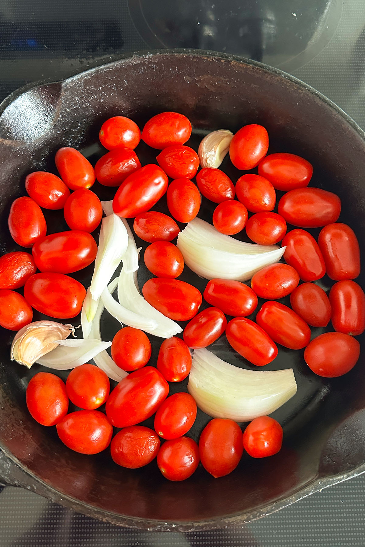 Onion and grape tomatoes in a cast iron skillet.