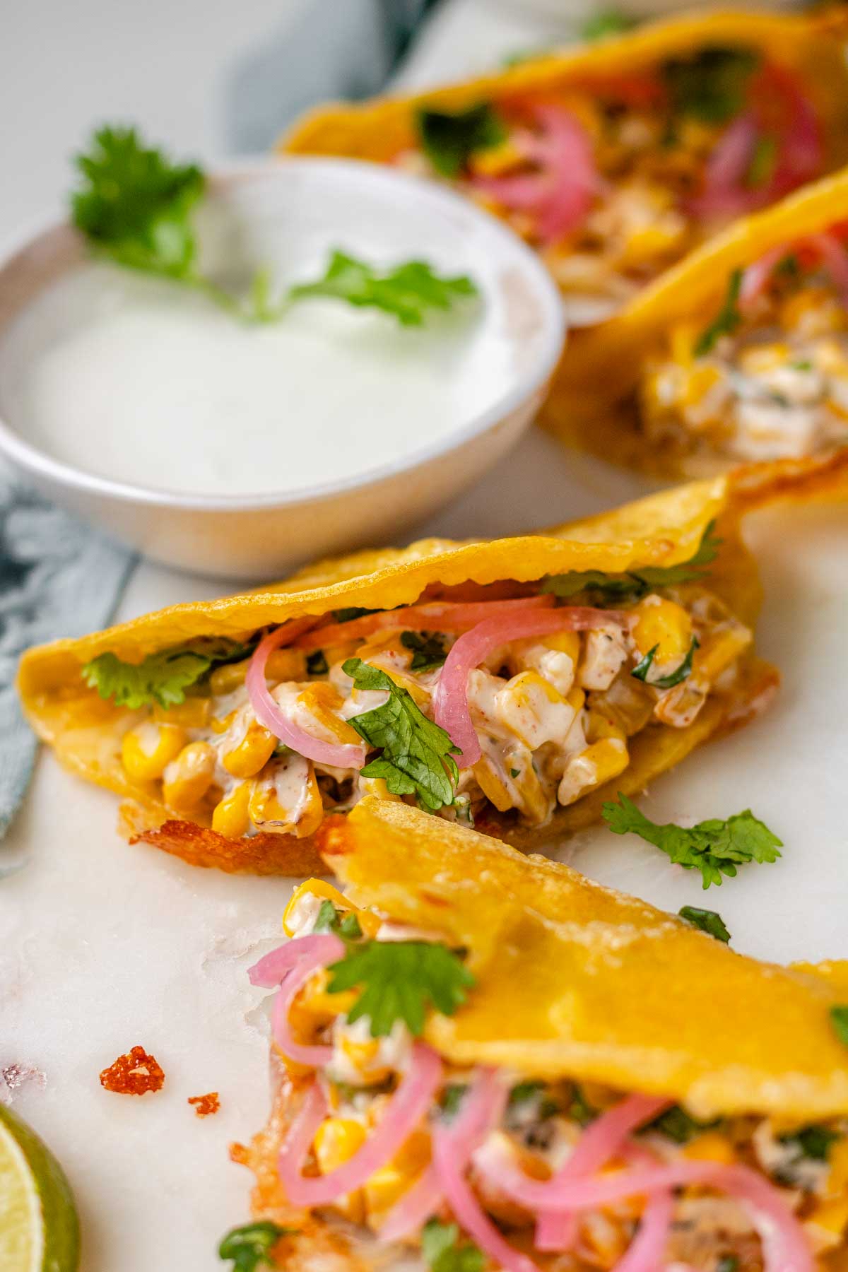 Cheesy crispy corn tacos on a white platter with garlic lime crema and pickled onions and lime wedges.