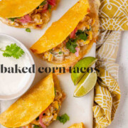 Cheesy crispy corn tacos on a white platter with garlic lime crema and pickled onions and lime wedges with the text baked corn tacos.