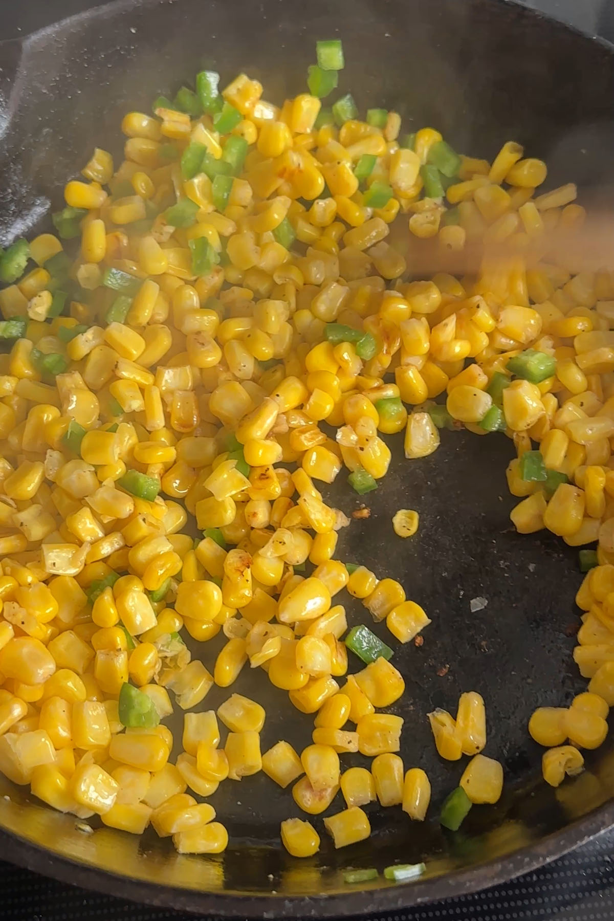 Corn and jalapeños are cooking in a cast-iron skillet.