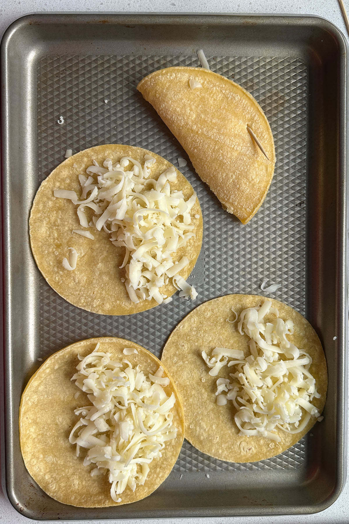 Cheese on corn tortillas on a baking sheet.