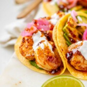 Hot honey Cajun shrimp tacos on a white platter with garlic lime crema and pickled onions.