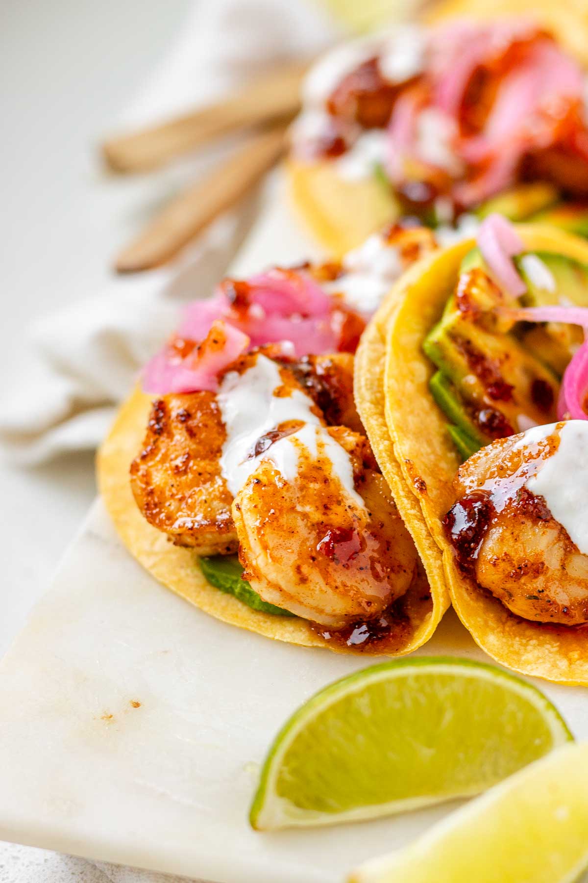 Hot honey Cajun shrimp tacos on a white platter with garlic lime crema and pickled onions.