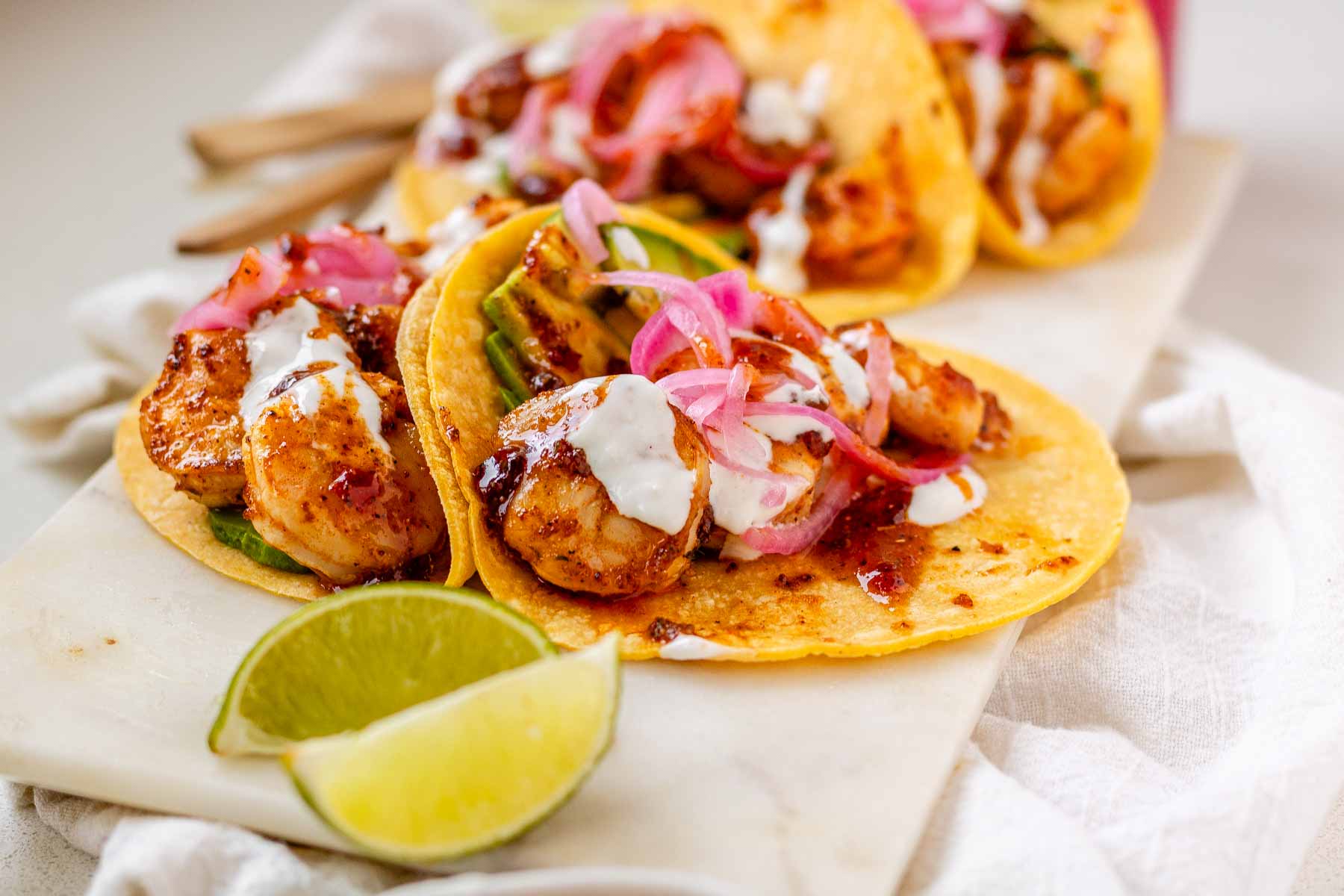 Hot honey Cajun shrimp tacos on a white platter with garlic lime crema and pickled onions.