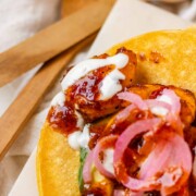 Hot honey Cajun shrimp tacos on a white platter with garlic lime crema and pickled onions.