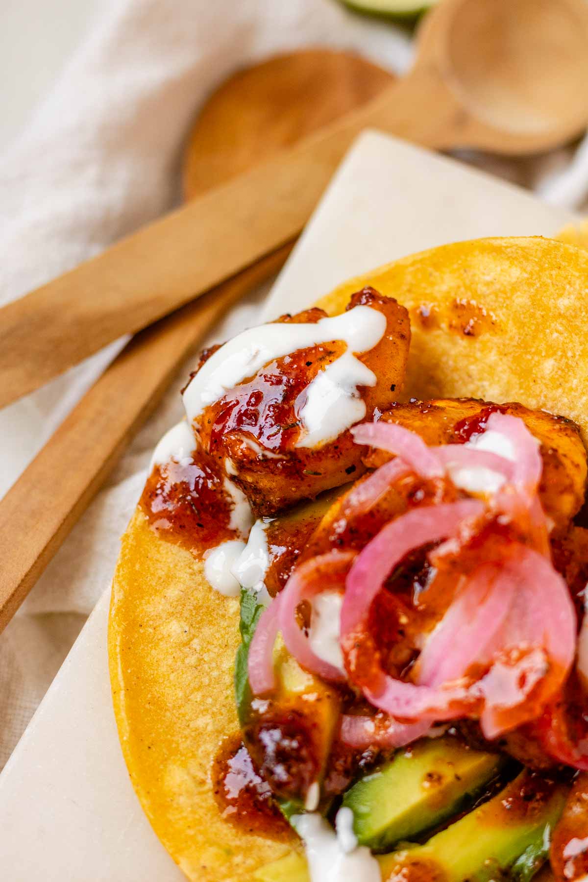 Hot honey Cajun shrimp tacos on a white platter with garlic lime crema and pickled onions.