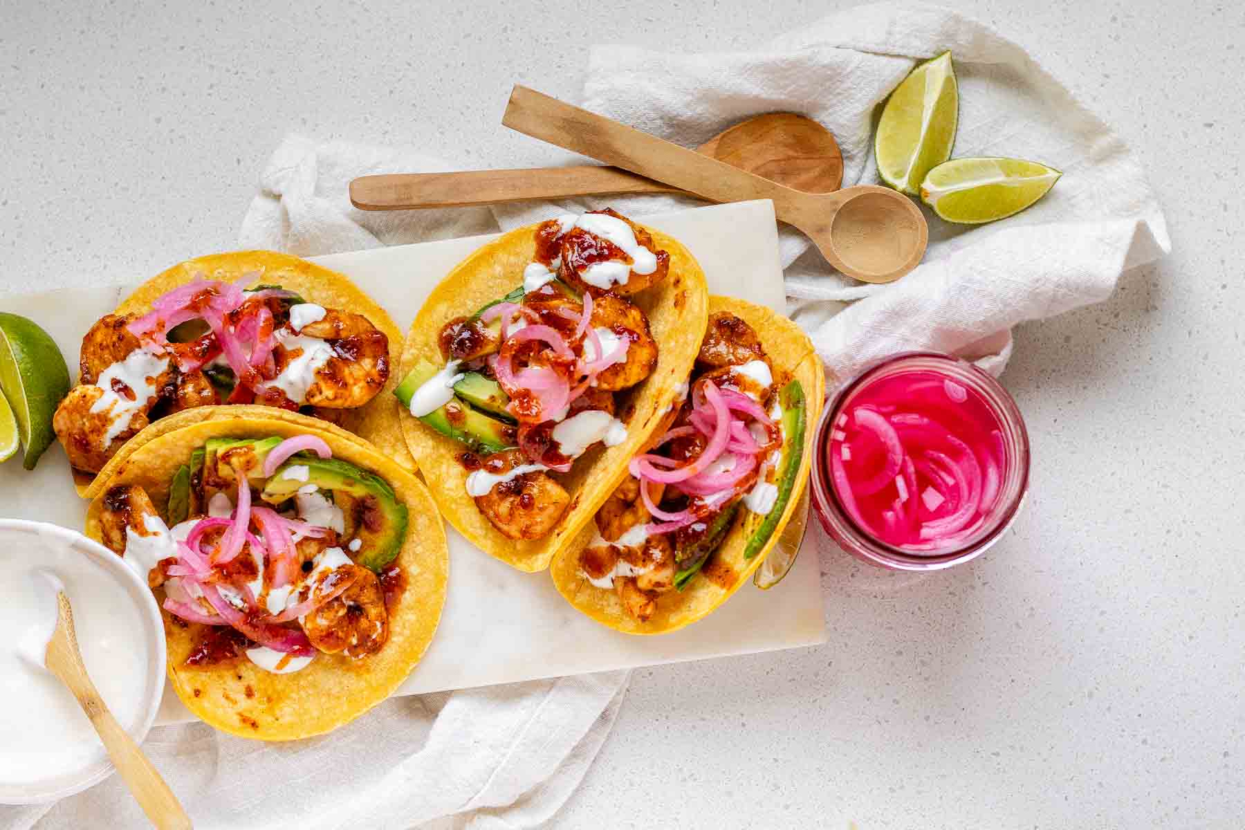 Hot honey Cajun shrimp tacos on a white platter with garlic lime crema and pickled onions.