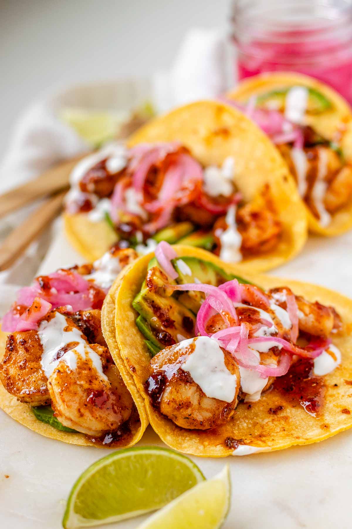 Hot honey Cajun shrimp tacos on a white platter with garlic lime crema and pickled onions.