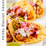 Hot honey Cajun shrimp tacos on a white platter with garlic lime crema and pickled onions with the text hot honey shrimp tacos.