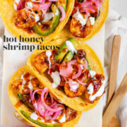 Hot honey Cajun shrimp tacos on a white platter with garlic lime crema and pickled onions with the text hot honey shrimp tacos.