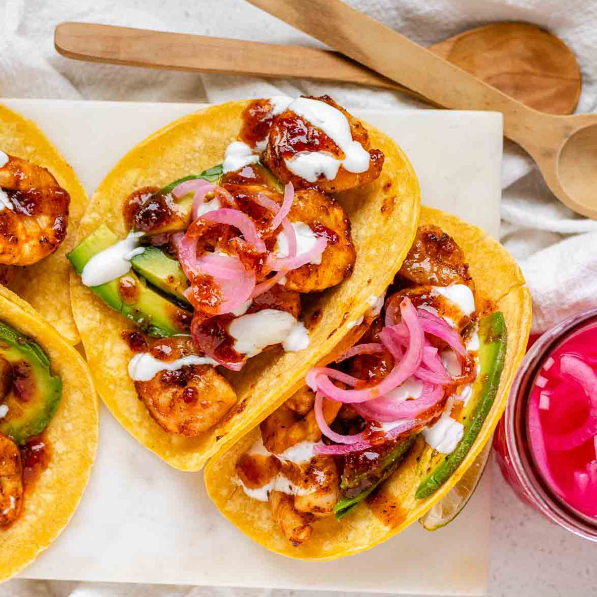 Hot honey Cajun shrimp tacos on a white platter with garlic lime crema and pickled onions.