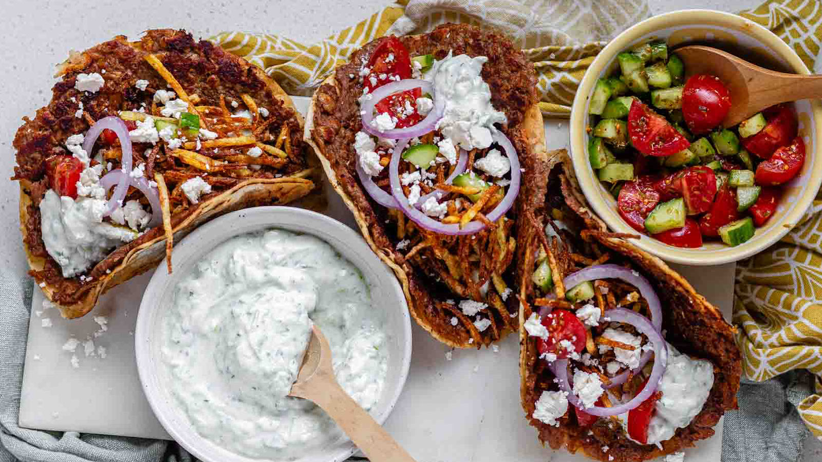 Tacos filled with meat, tomato, cucumber, red onion, feta, white sauce, and shoestring fries.