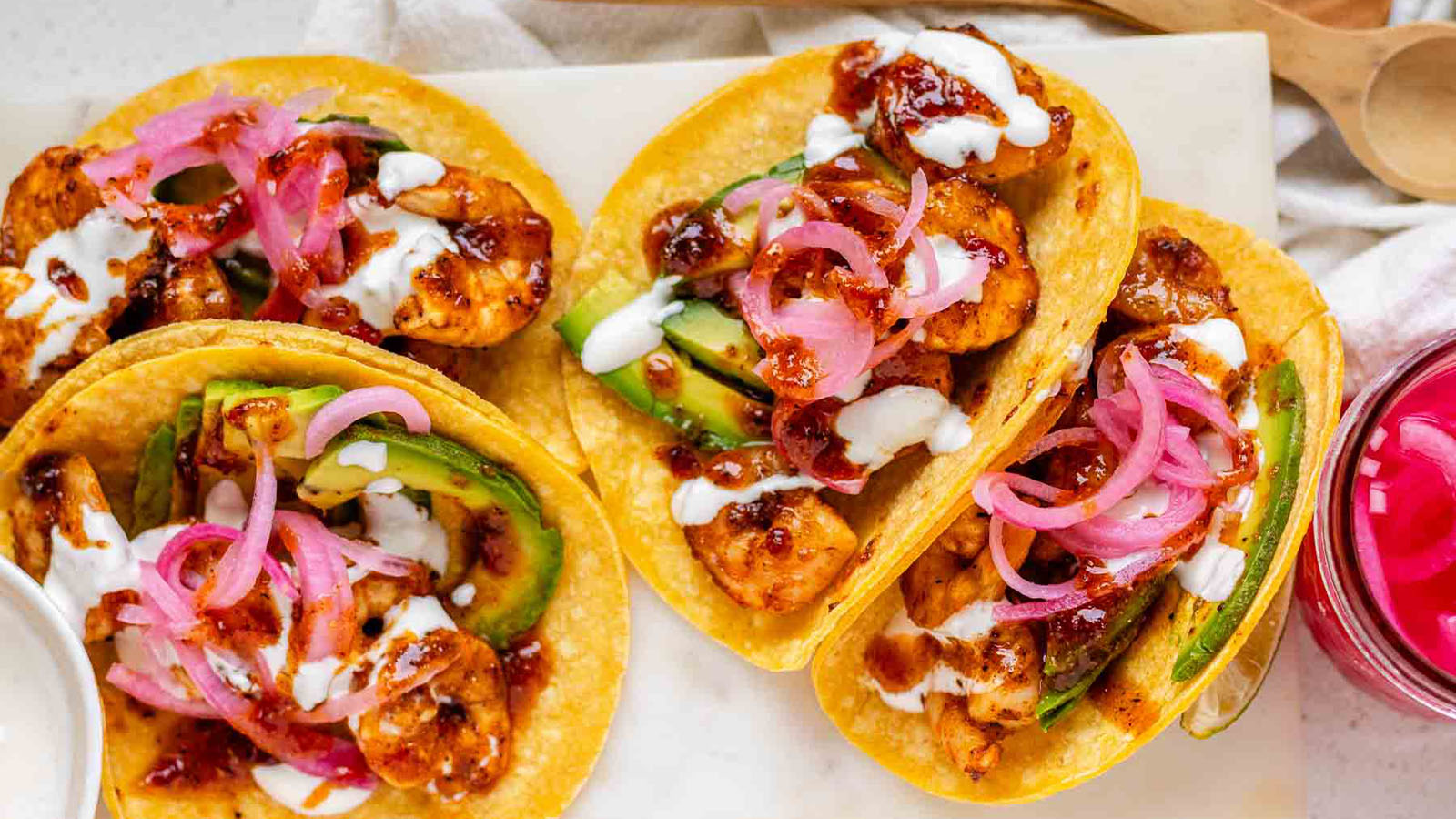 Hot honey Cajun shrimp tacos on a white platter with garlic lime crema and pickled onions.