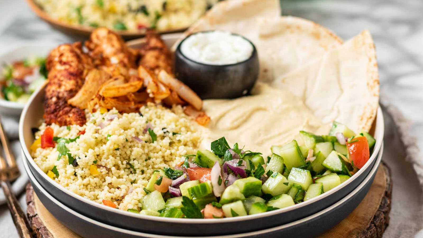 A chicken shawarma plate with chicken, pita, sauces, couscous and cucumber salad.
