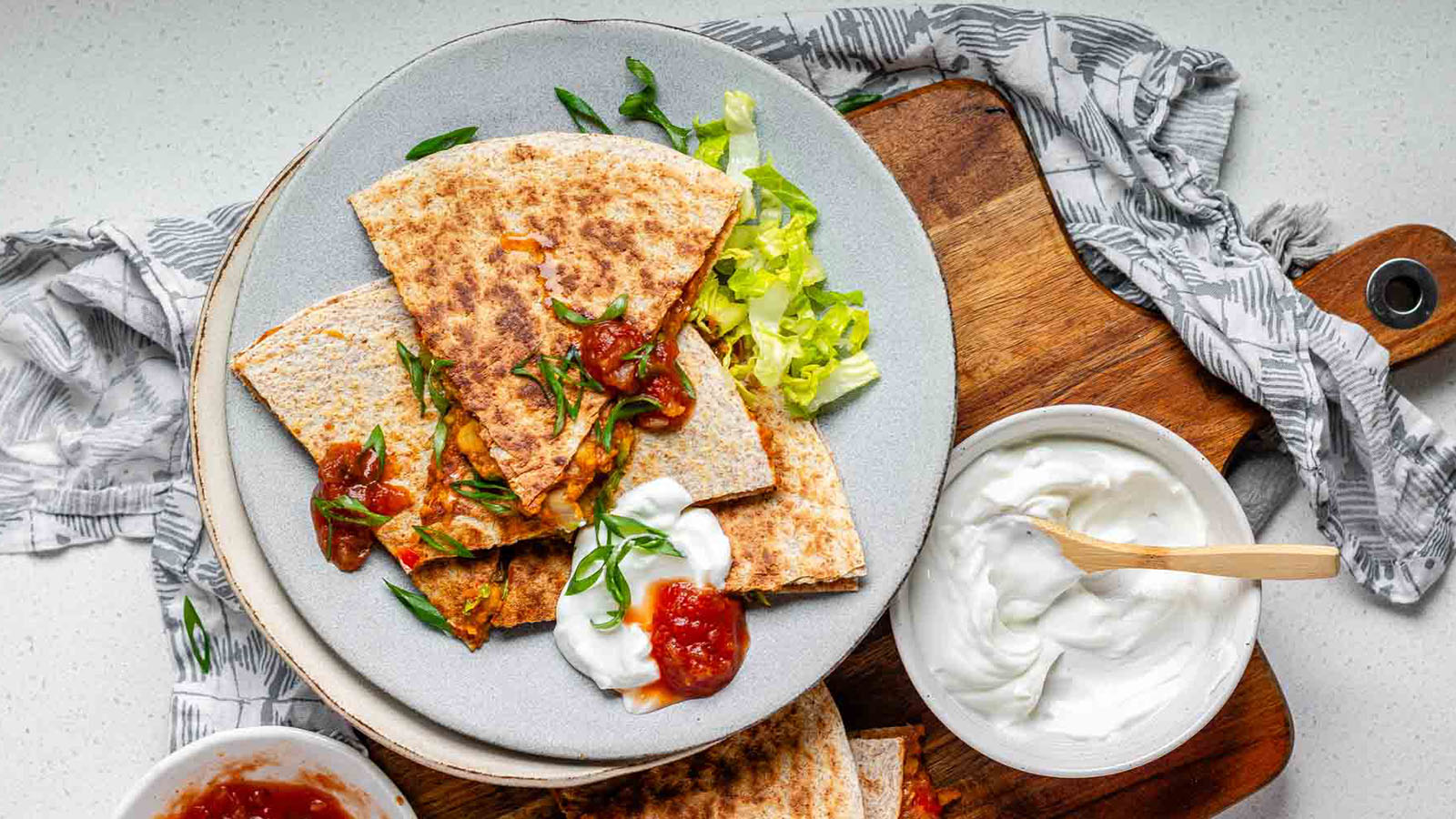 A quesadilla on a wooden board, cut into 6 slices and topped with lettuce.