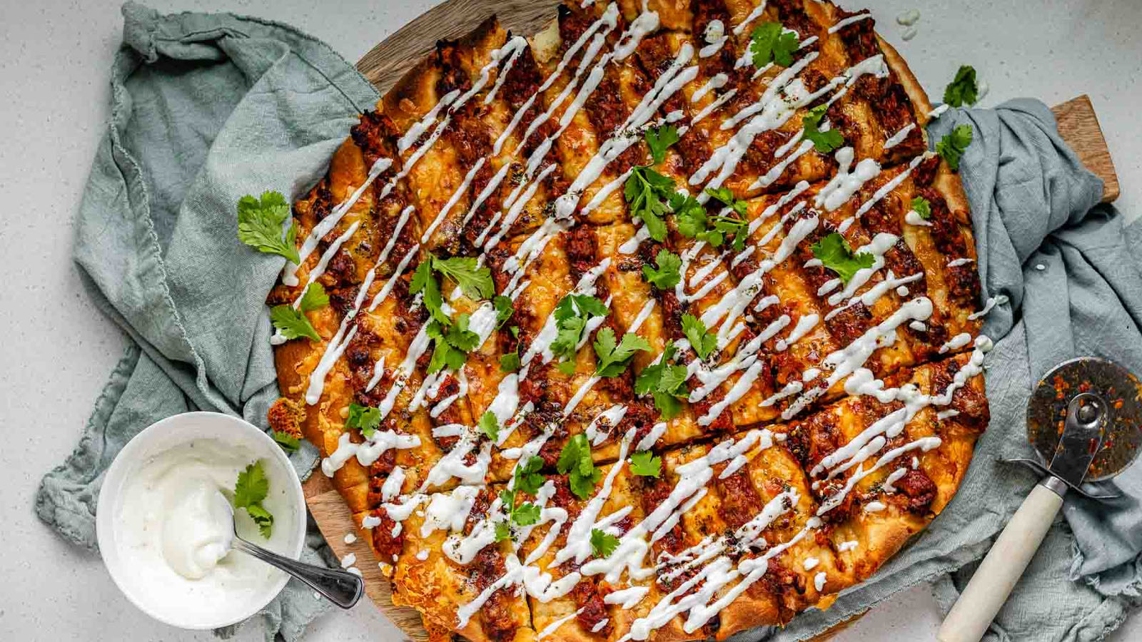 Flatbread topped with lines of cooked meat and cheese, drizzled with yogurt sauce, and scattered with cilantro leaves.