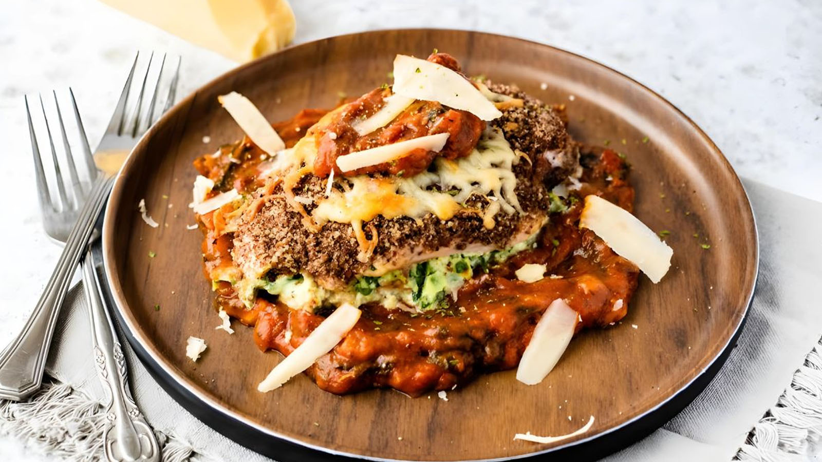 A chicken breast stuffed with cheese and spinach on tomato sauce with a crusted exterior and tomato and cheese on top.