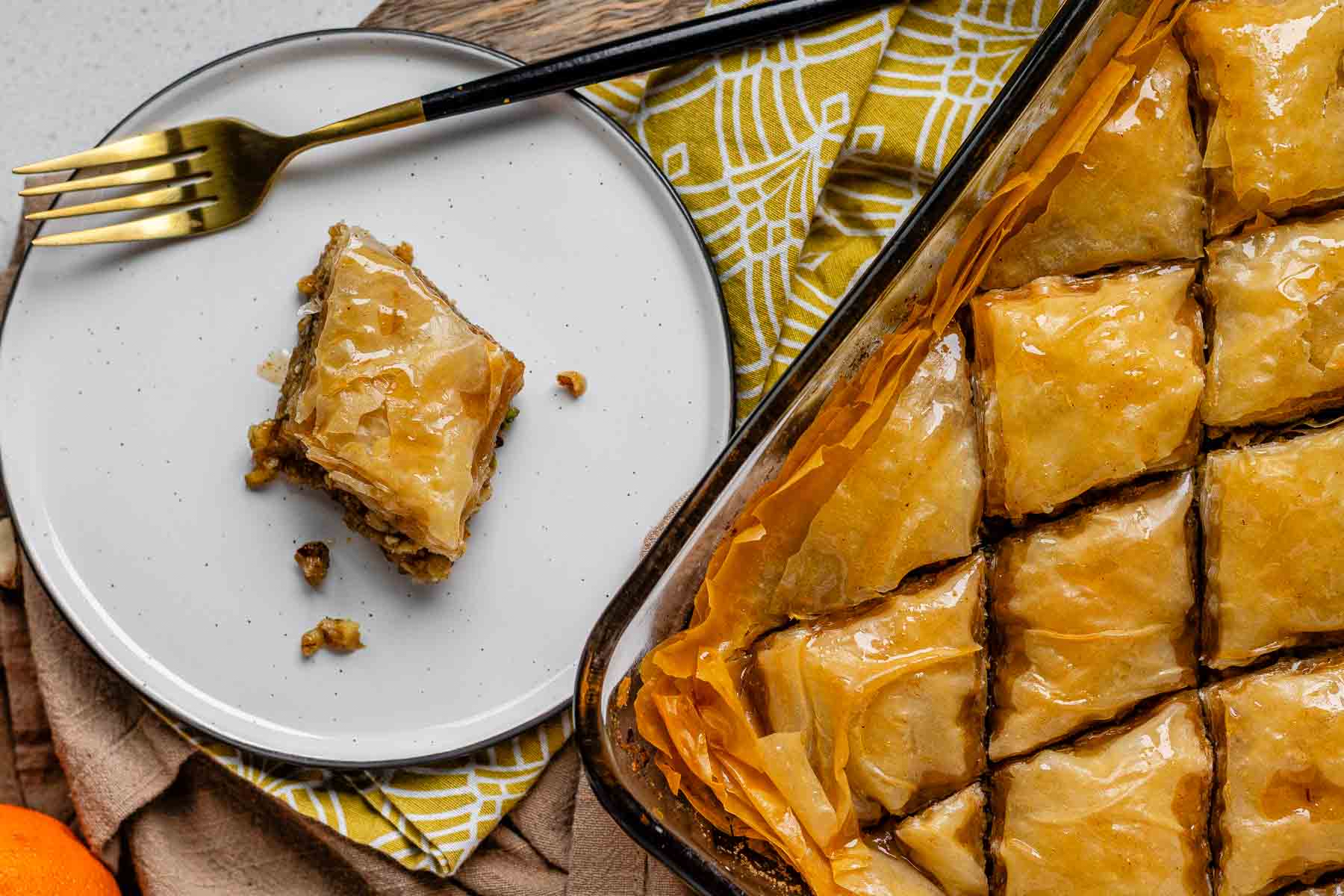 A slice of flaky, nutty pastry on a plate beside a baking dish of diamond-cut flaky pastry.
