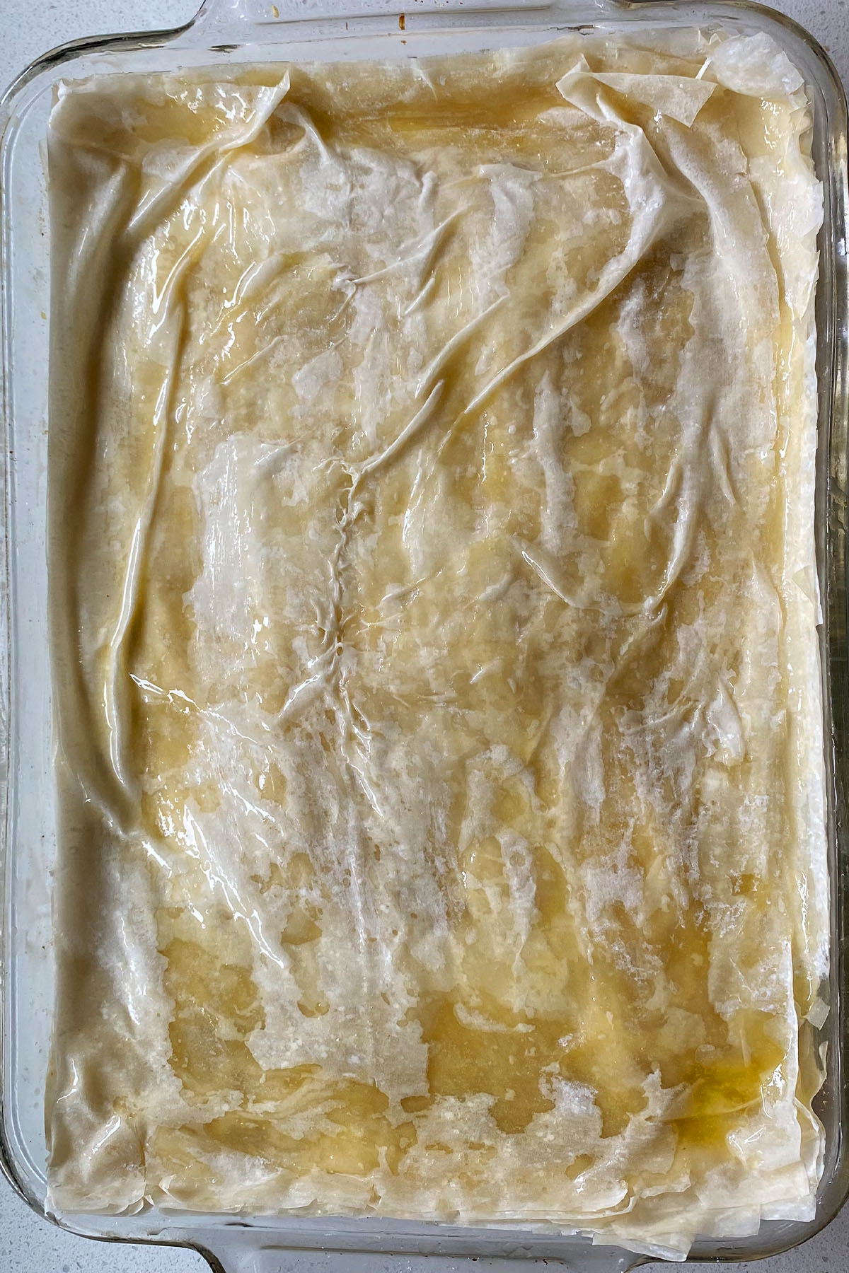 Layered buttered phyllo dough in a 9x13 baking dish for baklava.