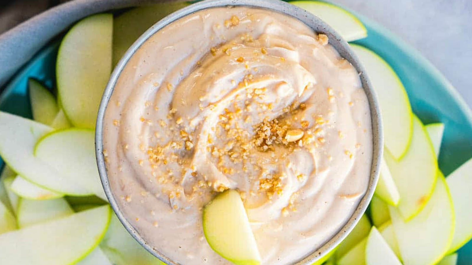 Peanut butter dip in a bowl surrounded by apple slices.