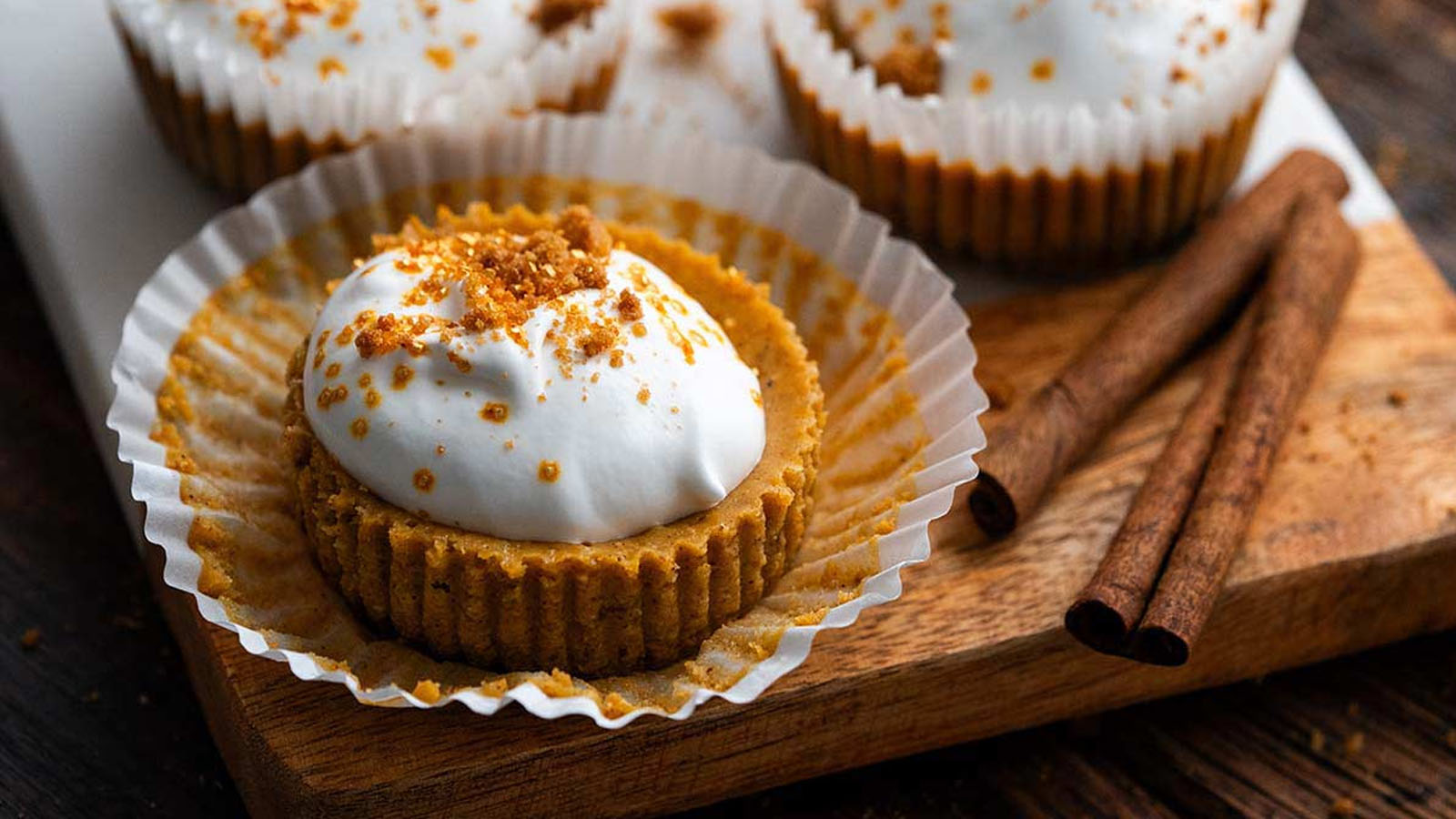 A bite sized dessert on a muffin paper topped with whipped cream and graham crumbs.
