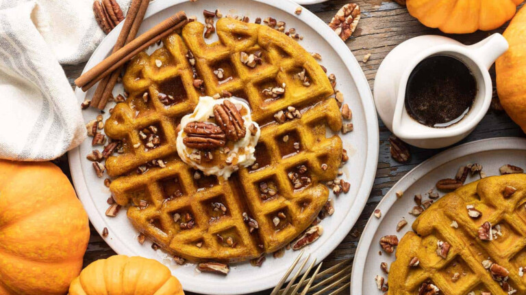 Waffles on plates topped with butter, syrup, and pecans.