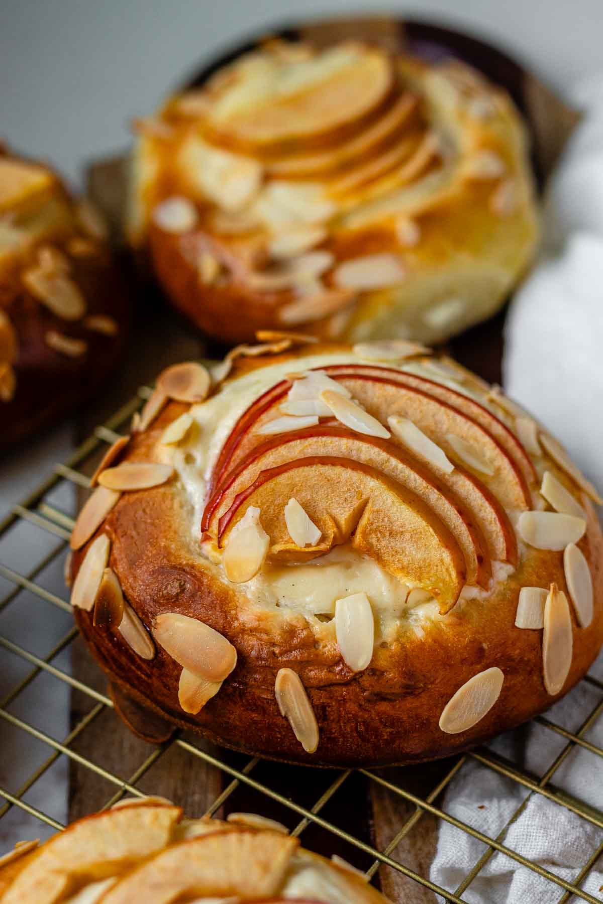 Apple and almond sweet brioche buns topped with sliced apples, cream cheese, and toasted almonds on a baking sheet.