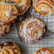 Apple and almond sweet brioche buns topped with sliced apples, cream cheese, powdered sugar, and toasted almonds on a baking sheet with the text apple sweet brioche buns.