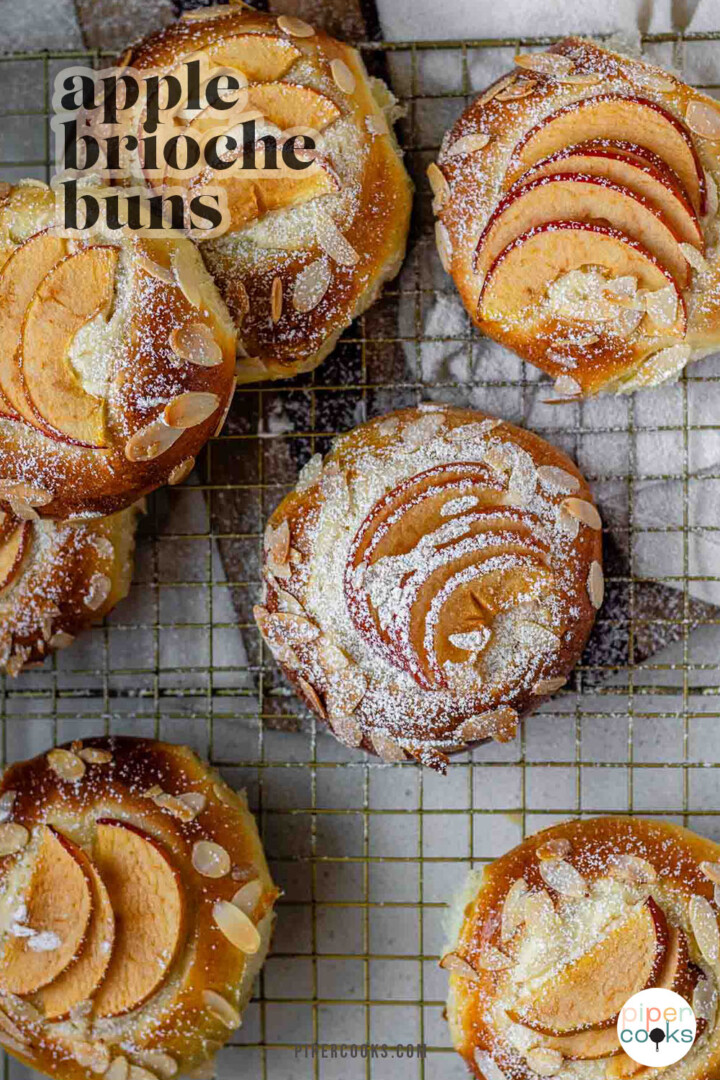 Apple and almond sweet brioche buns topped with sliced apples, cream cheese, powdered sugar, and toasted almonds on a baking sheet with the text apple sweet brioche buns.