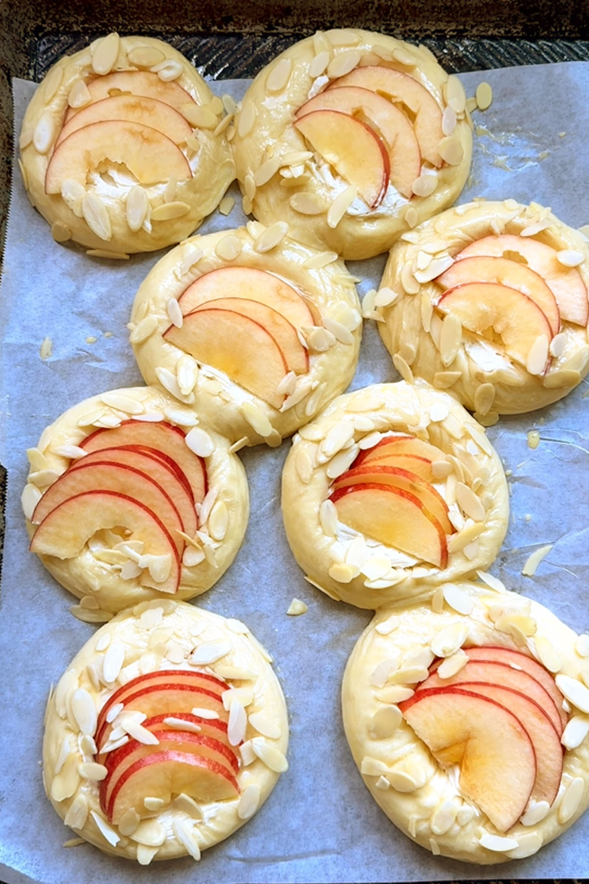 Unbaked sweet buns topped with cream cheese apple slices, and almonds.