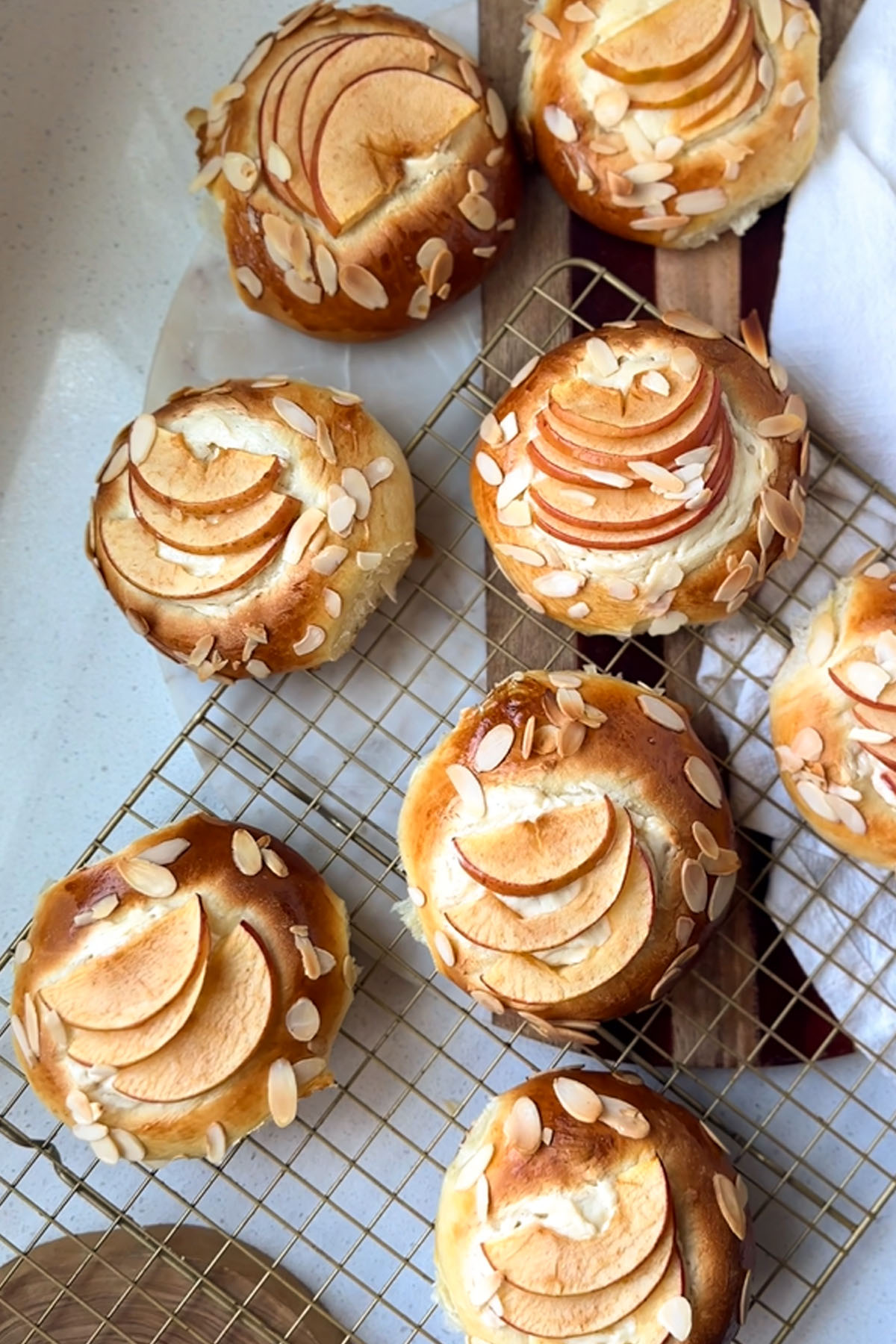 Apple and almond sweet brioche buns topped with sliced apples, cream cheese, and toasted almonds on a baking sheet.
