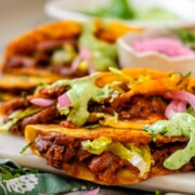 Tacos on a platter with a green sauce and pickled red onions.