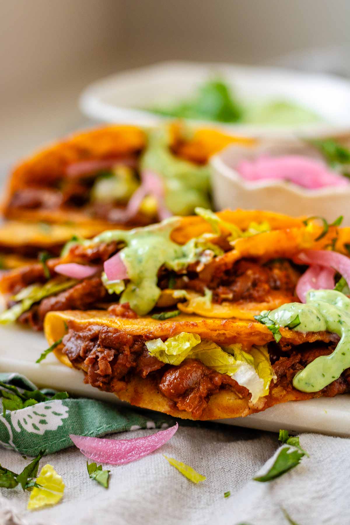Tacos on a platter with a green sauce and pickled red onions.