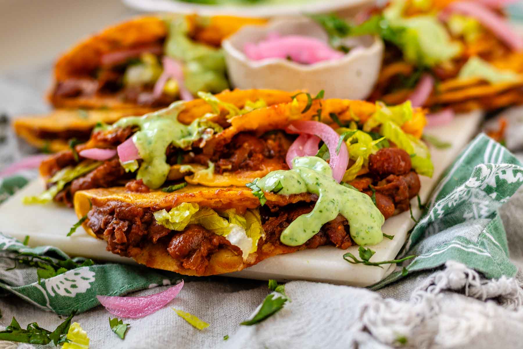 Tacos on a platter with a green sauce and pickled red onions.