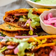 Tacos on a platter with a green sauce and pickled red onions.