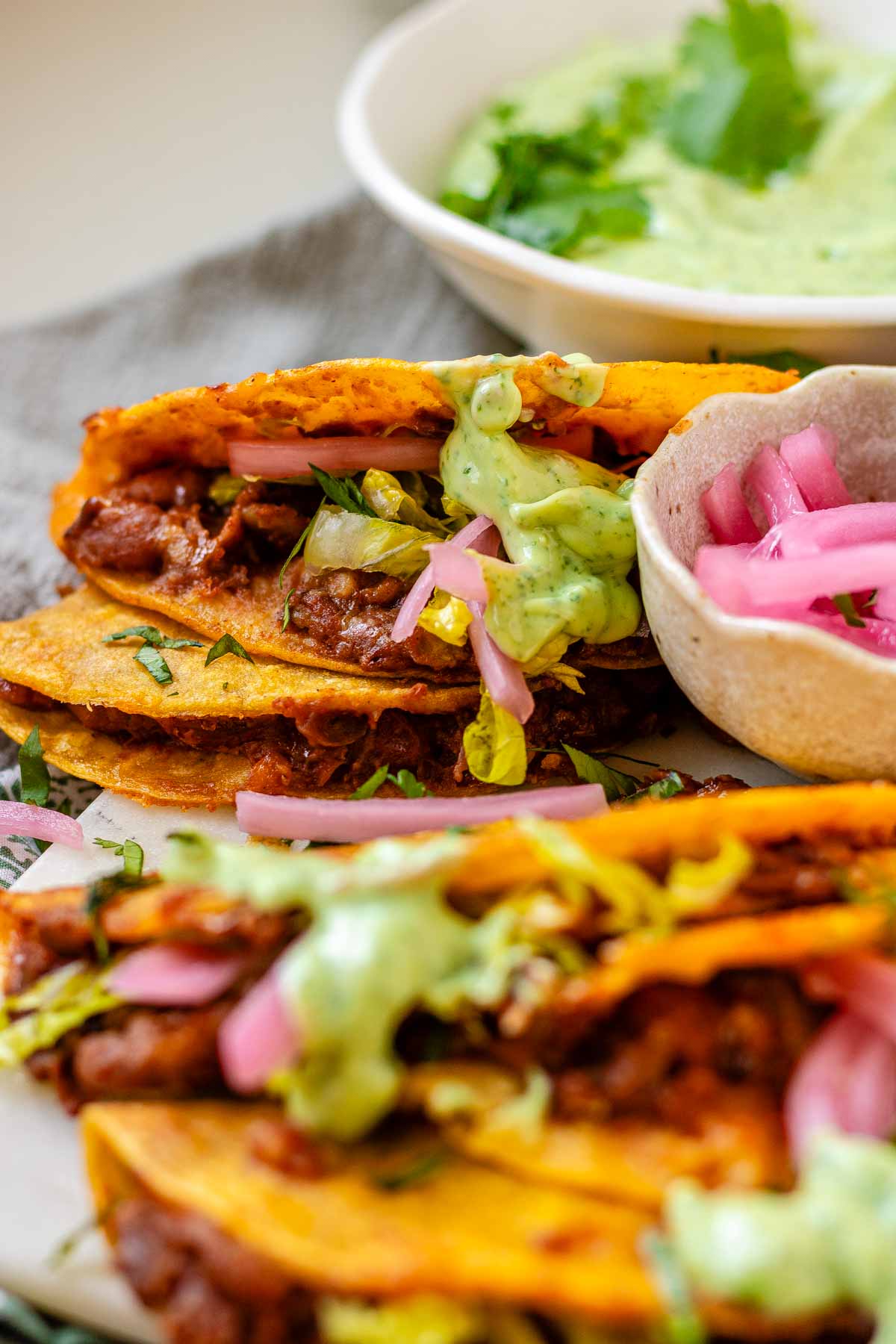 Tacos on a platter with a green sauce and pickled red onions.
