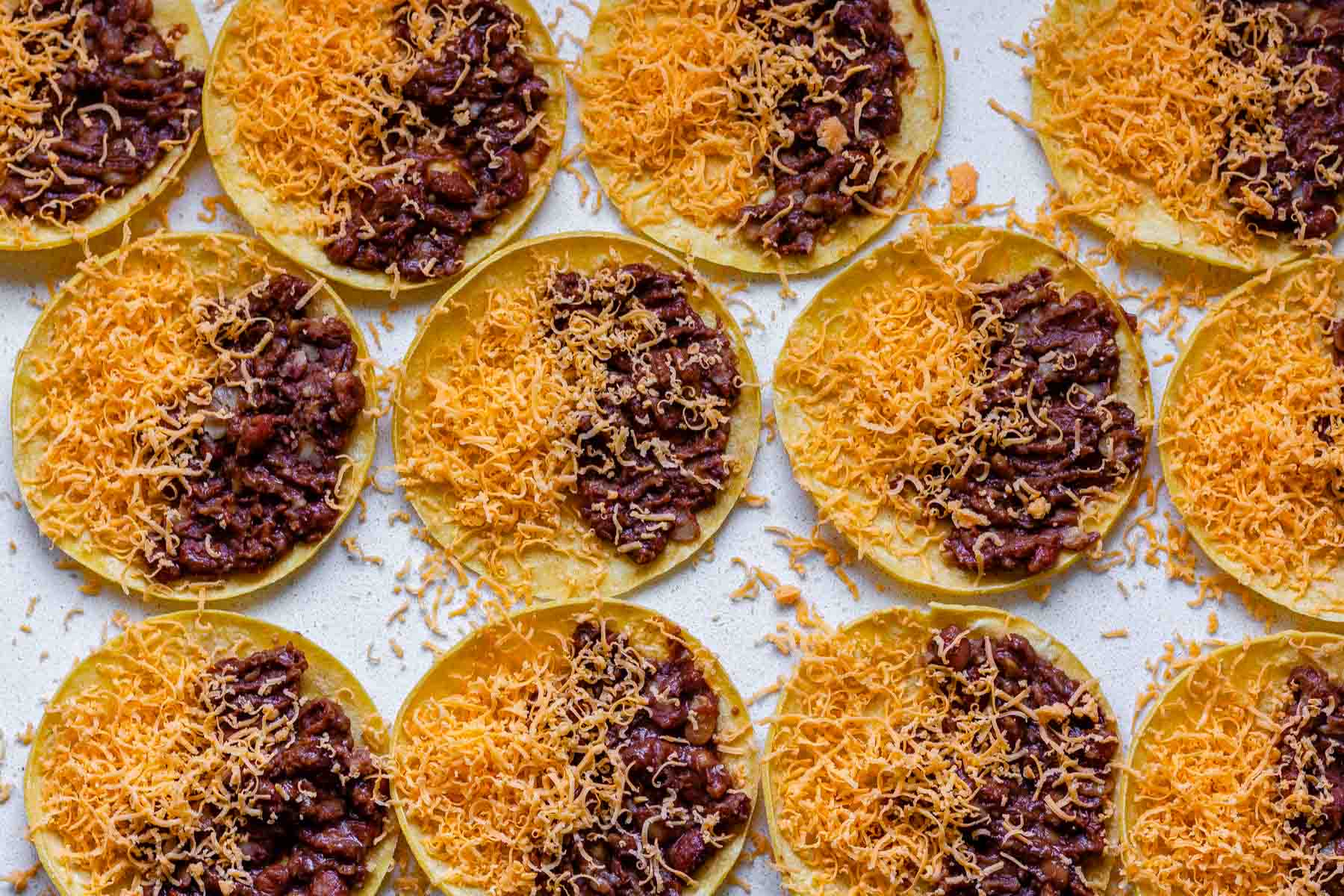 Corn tortillas with beans on one side and shredded cheddar on the other.
