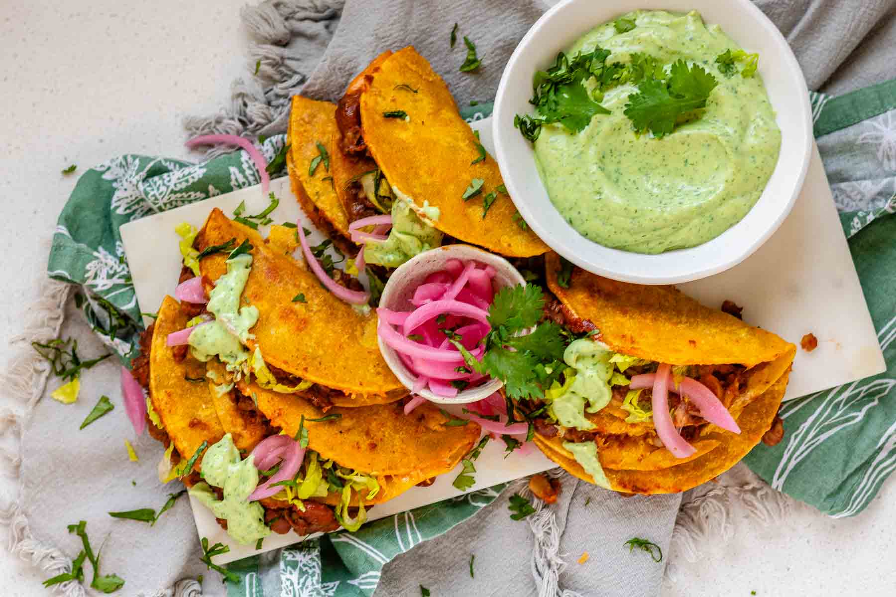 Tacos on a platter with a green sauce and pickled red onions.