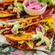 Tacos on a platter with a green sauce and pickled red onions.