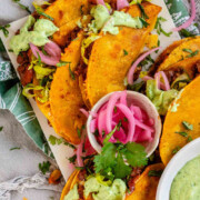 Tacos on a platter with a green sauce and pickled red onions with the text crispy bean tacos.