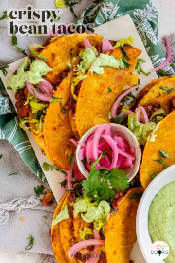 Tacos on a platter with a green sauce and pickled red onions with the text crispy bean tacos.