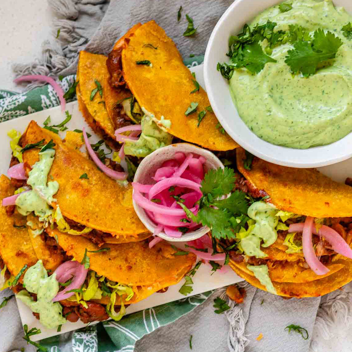Tacos on a platter with a green sauce and pickled red onions.