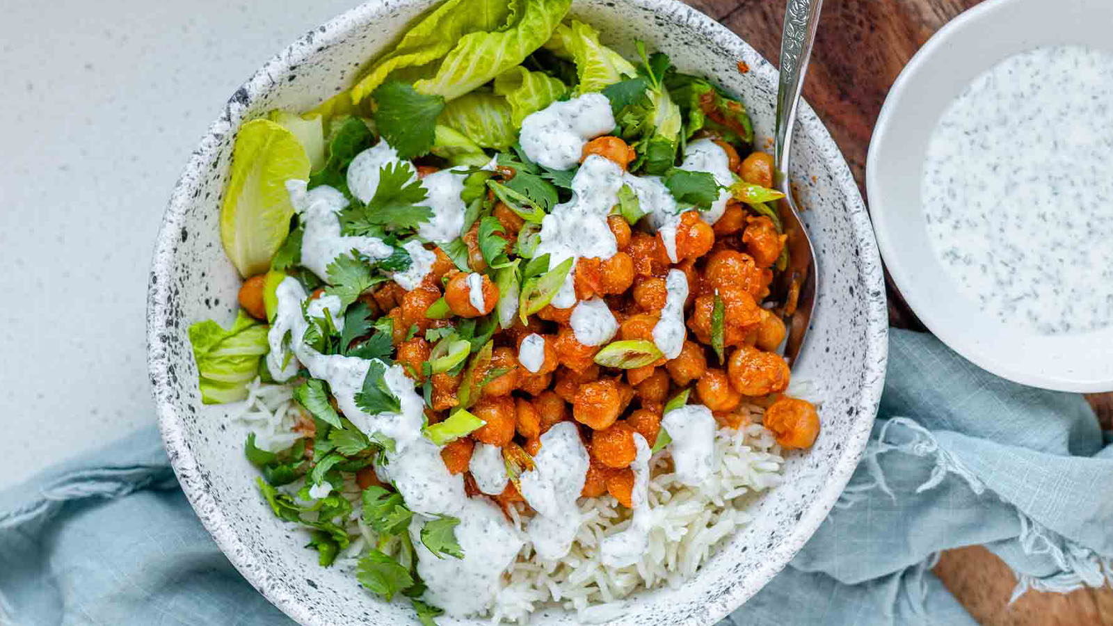 A bowl with rice, saucy chickpeas, lettuce, chopped herbs and white herby sauce.