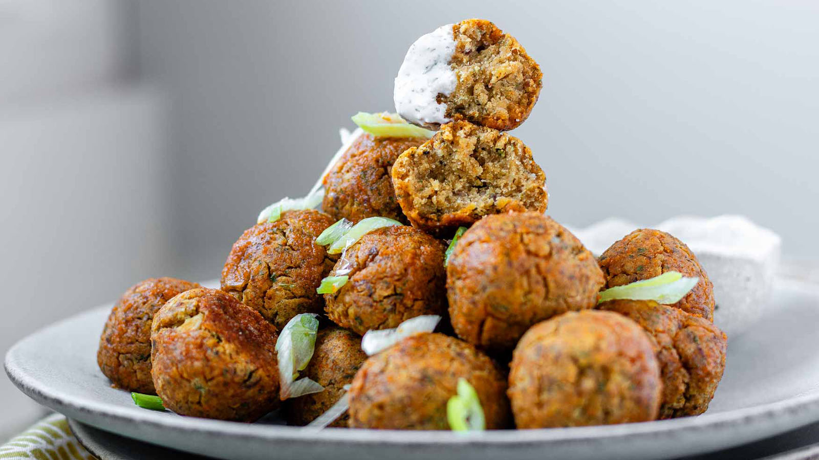 Stacked veggie meatballs on a plate garnished with a white sauce and sliced green onions.