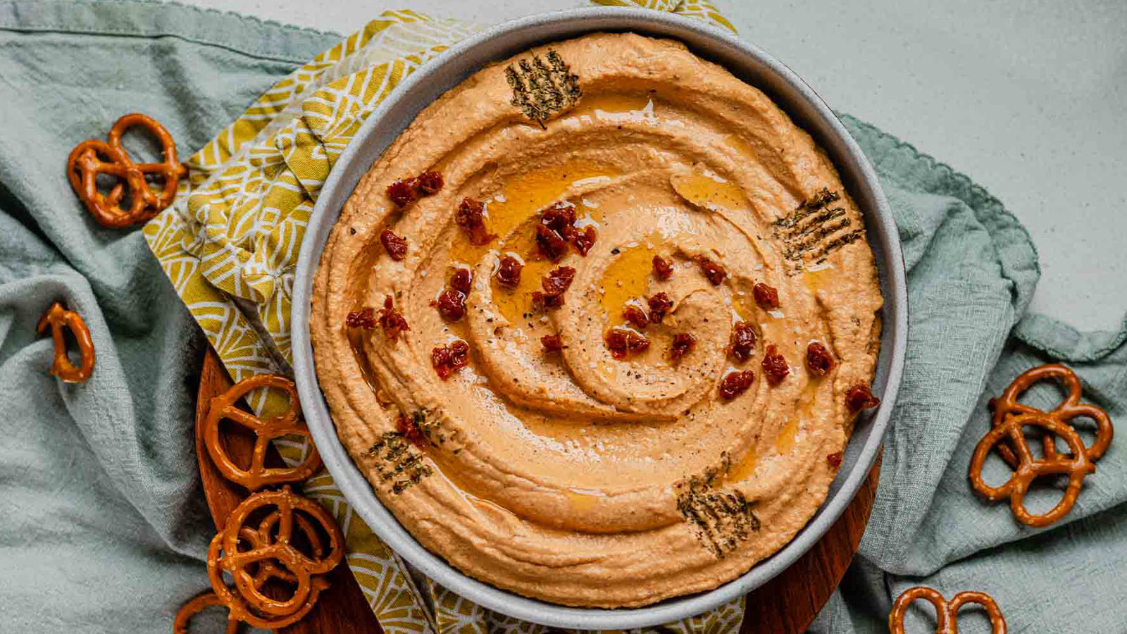 Hummus in a bowl topped with chopped sundried tomatoes, olive oil and dried spices.