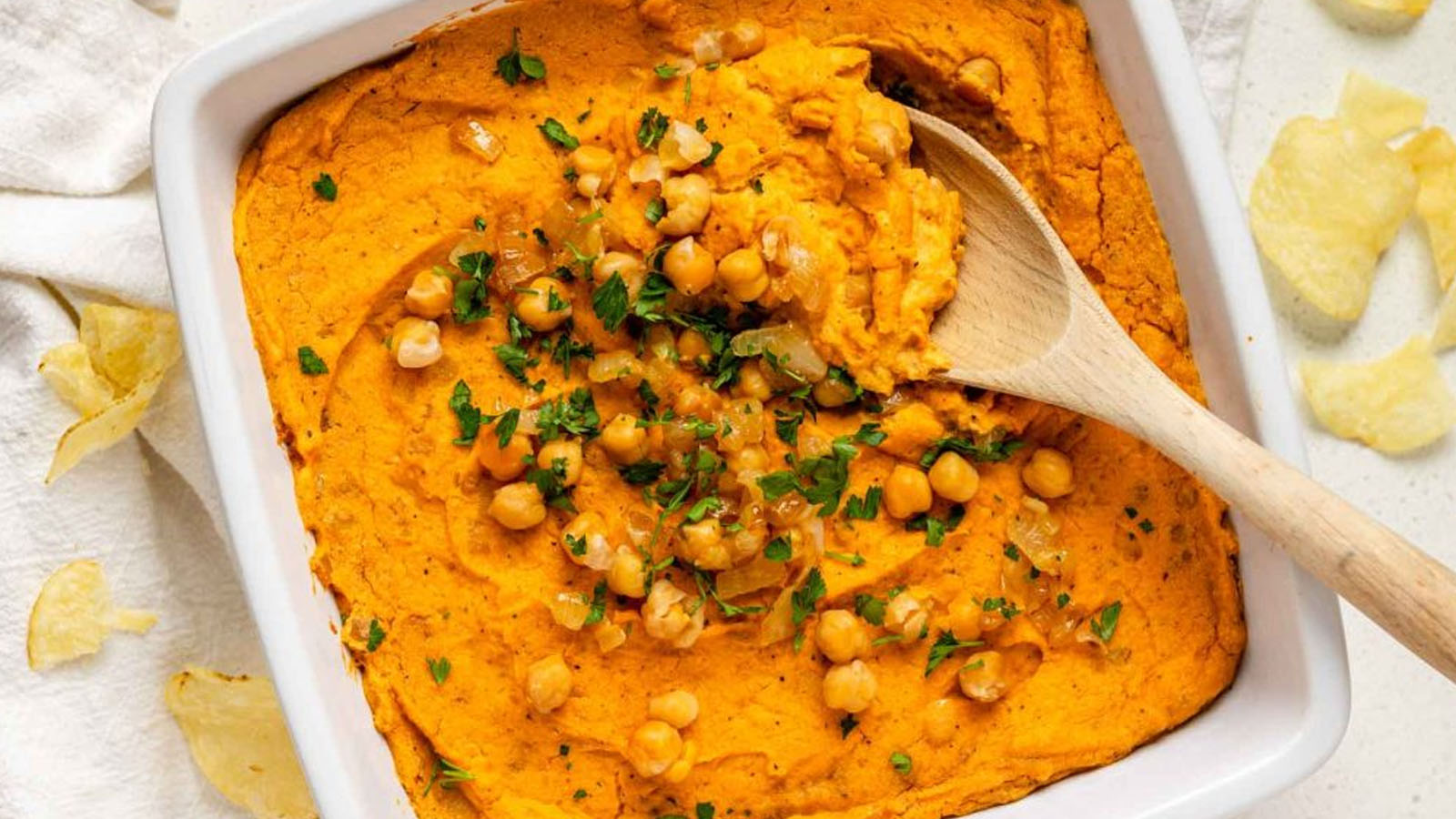 And orange dip in a baking dish topped with chickpeas and chopped herbs.
